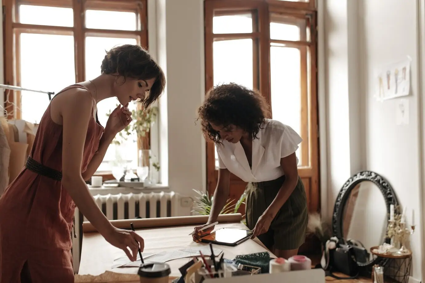 おしゃれな夏の装いをしたクールな若い女性たちがファッションデザイナーとして働いている。赤いドレスの少女と白いブラウスの女性がクラフト紙のシートに服の型紙を描いている。